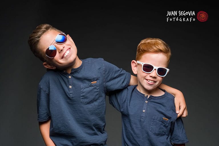 Fotografía para reportaje de comunión en estudio de dos hermanos sonrientes con gafas de sol en el estudio del fotógrafo Juan Segovia en Tarragona