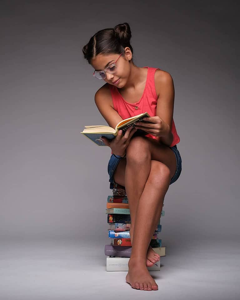 Fotografía en estudio para el book de la actriz Jasmine Serra con gafas leyendo sentada sobre una pila de libros
