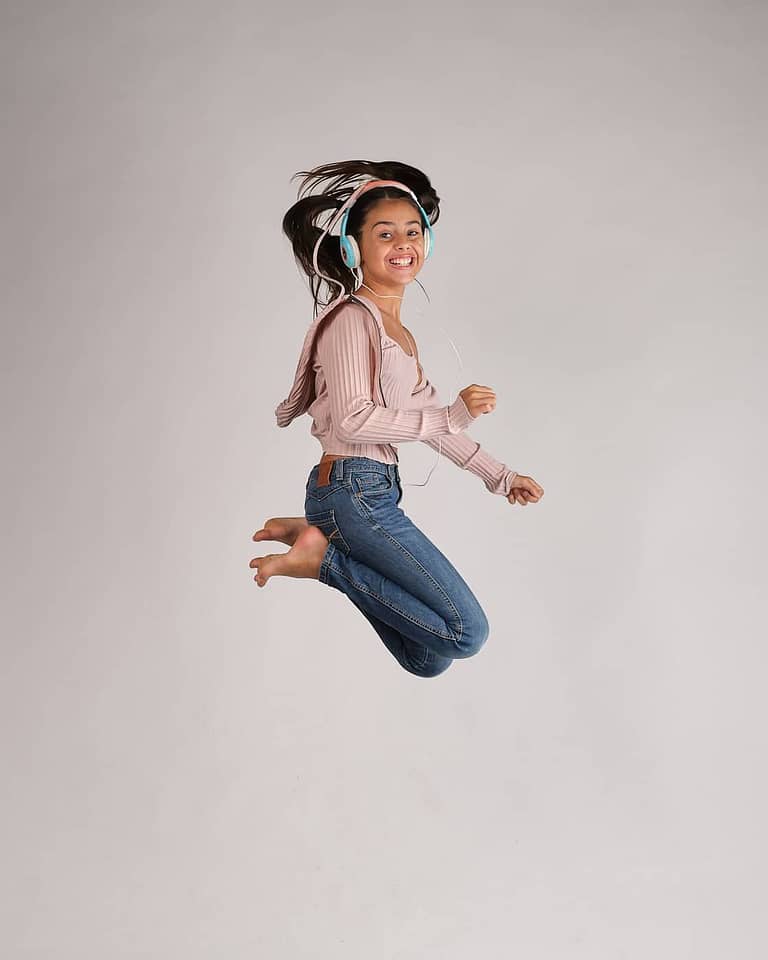 Fotografia para el book de la actriz Jasmine Serra saltando y sonriendo con coletas y auriculares
